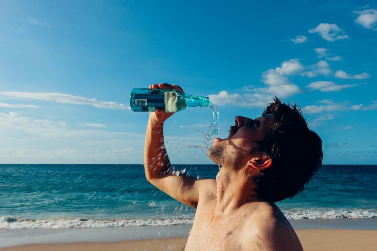 man drinking water after tanning to rehydrate his skin